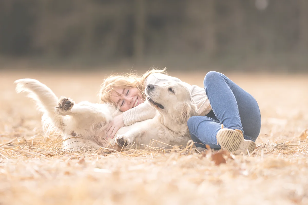 Een vrouw ligt met haar golden retriever in het gras, op een foto van Dierapotheker